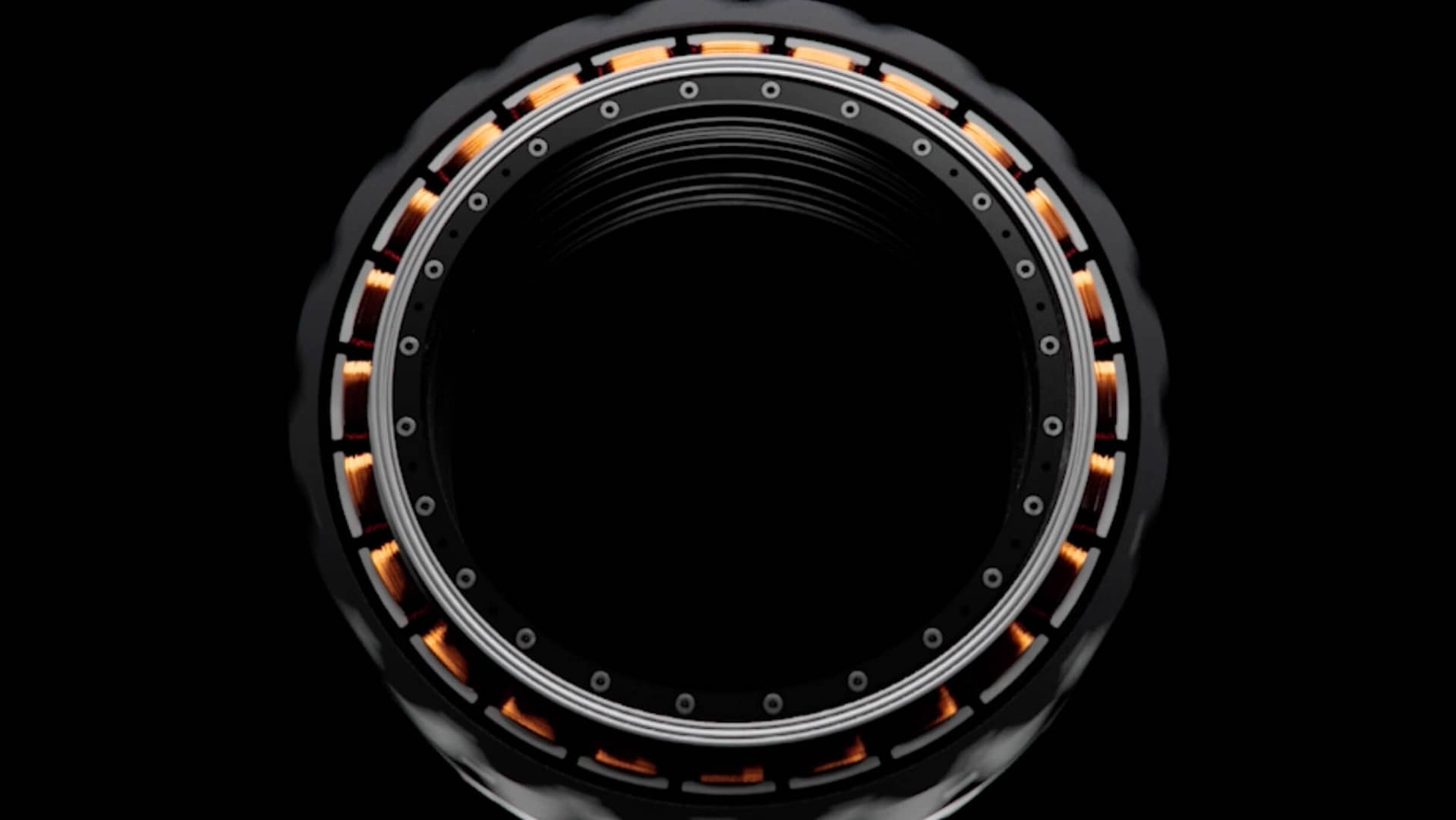 A close-up of a circular mechanical component with a black center and intricate details. Orange elements and several small screws or bolts are evenly spaced around its circumference, resembling a lens or turbine. The background is entirely black.