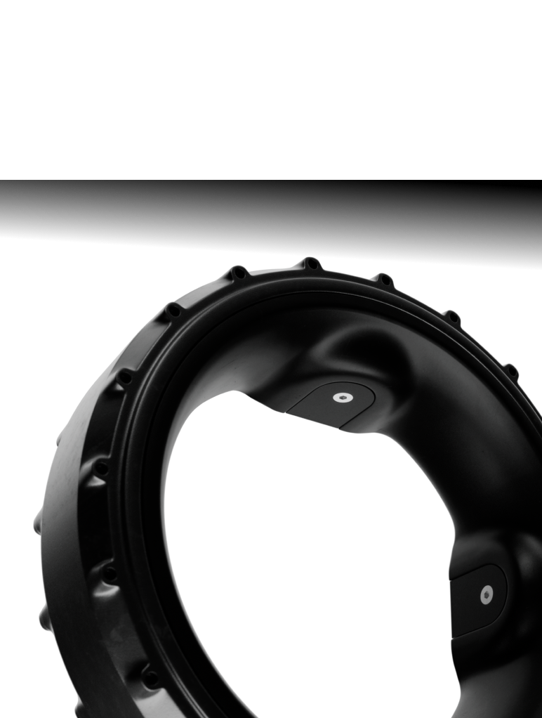 Close-up of a black circular mechanical component with a smooth, glossy surface and evenly spaced raised edges, against a white background. The interior features geometric design elements with circular patterns.
